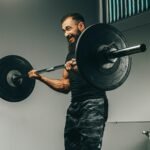 Muscular man in black sportswear lifting barbell in a gym