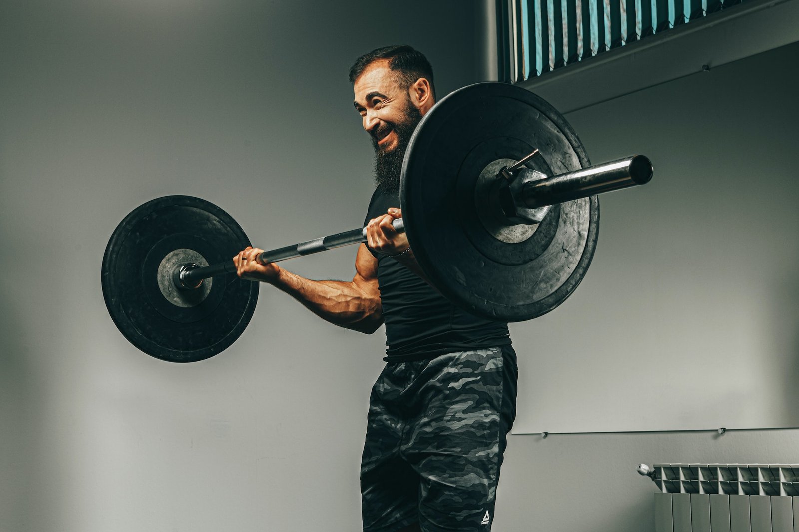 Muscular man in black sportswear lifting barbell in a gym